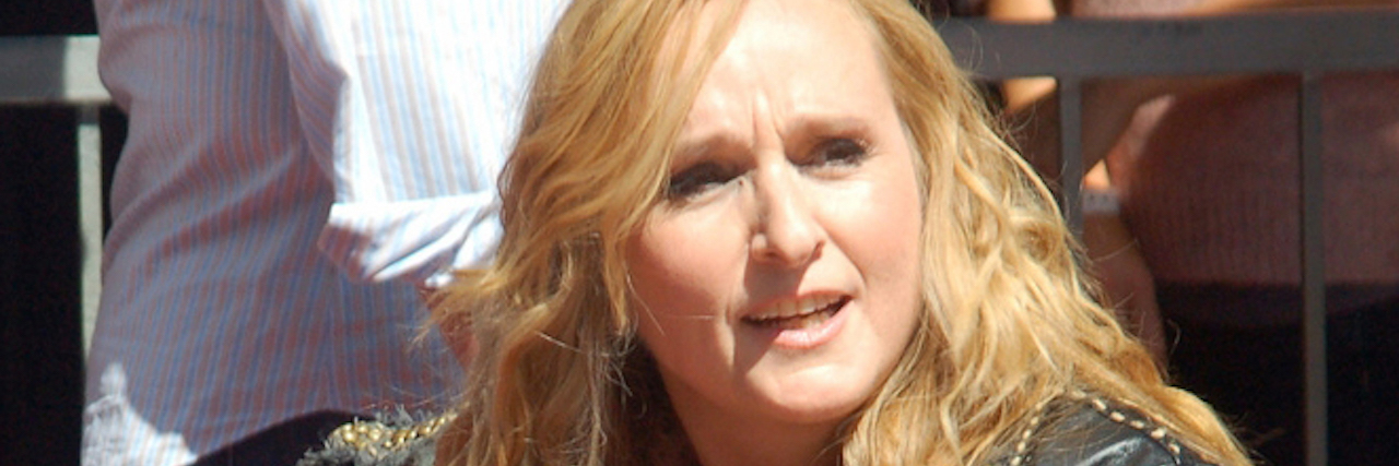 What Melissa Etheridge Most Wants Others to Know About Addiction Melissa Etheridge, a woman with long blonde hair, wears a letter jacket and plays an acoustic guitar