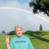 photo of the contributor Conor Bezane in Hawaii, making a peace sign with his hand, posing underneath a double rainbow