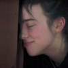 screenshot from Billie Eilish documentary showing her leading her forehead against door frame, eyes closed and smiling