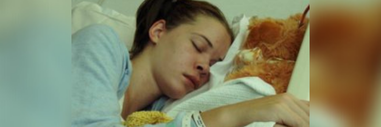Photo of author, a young white woman with brown hair, lying in a hospital bed after surgery asleep