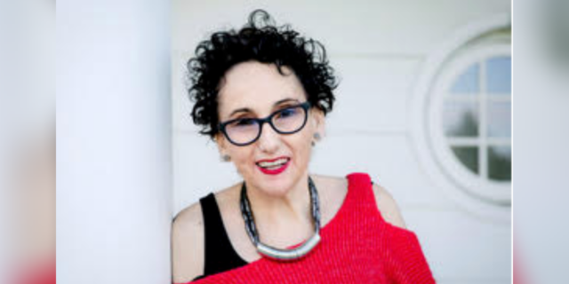 photo of author; white woman smiling, short curly black hair wearing a red sweater