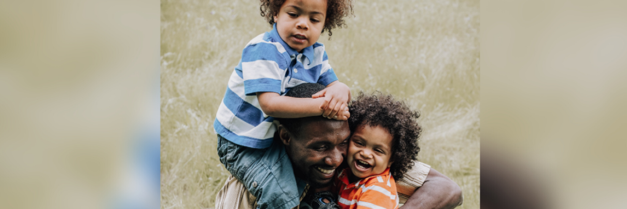 Black Generational Trauma Myths That Need to End photo of a Black father and two children, one in his arms and the other on his shoulder, laughing and smiling together