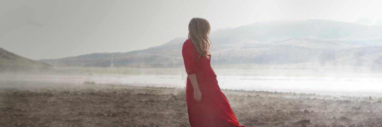 Being Chronically Ill and Suicidal During COVID-19 Let Me Help Others A blond white woman in a red dress looking over her shoulder at the ocean, standing on a beach