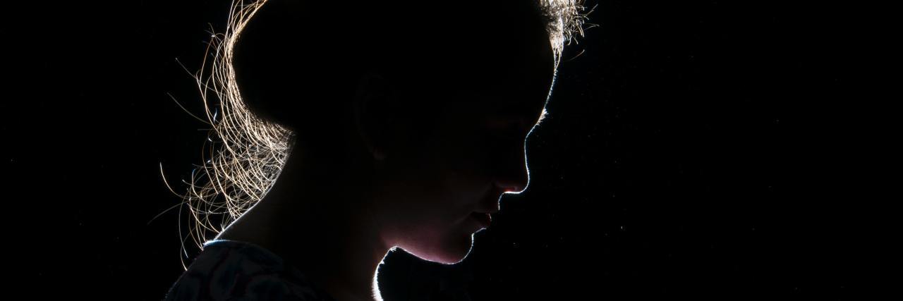 photo of a woman silhouetted in darkness, only the edge of her face and hair in profile can be seen