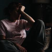 photo of woman sitting on couch, resting head in hand in almost darkness