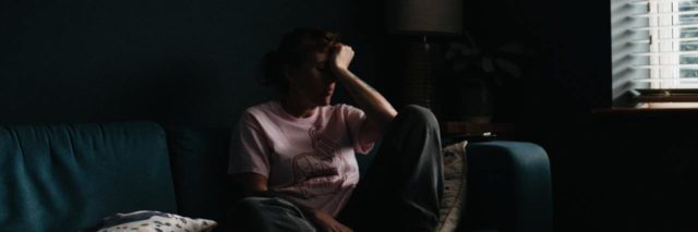 photo of woman sitting on couch, resting head in hand in almost darkness