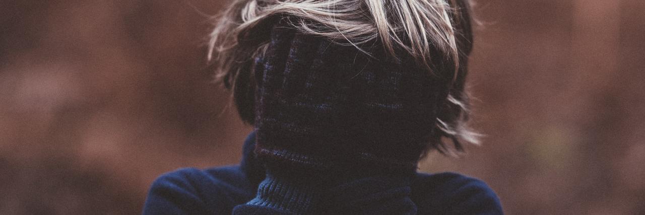 How My Childhood Loneliness Grew Into Anxiety photo of child with blonde hair, wearing gloves and covering face and eyes, posing in front of a blurry forest background