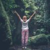 photo of woman in forest with her arms raised in happiness