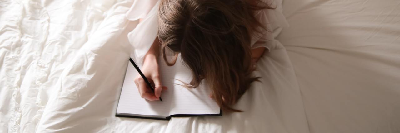 How a Gratitude List Can Help With Depression and Anxiety photo of woman lying on bed with white sheets, writing in journal