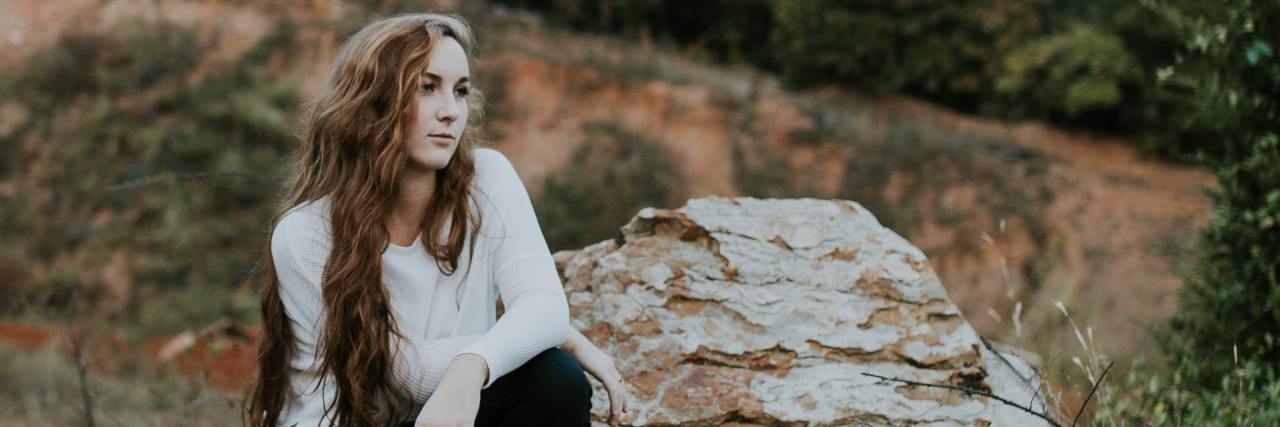 How to Know if You Have an 'Anxious Attachment Style' photo of a young woman sitting on a large rock on a slope, looking off into distance