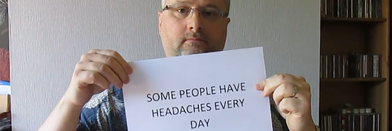 Andy holding a sign that says "Some people have headaches every day."