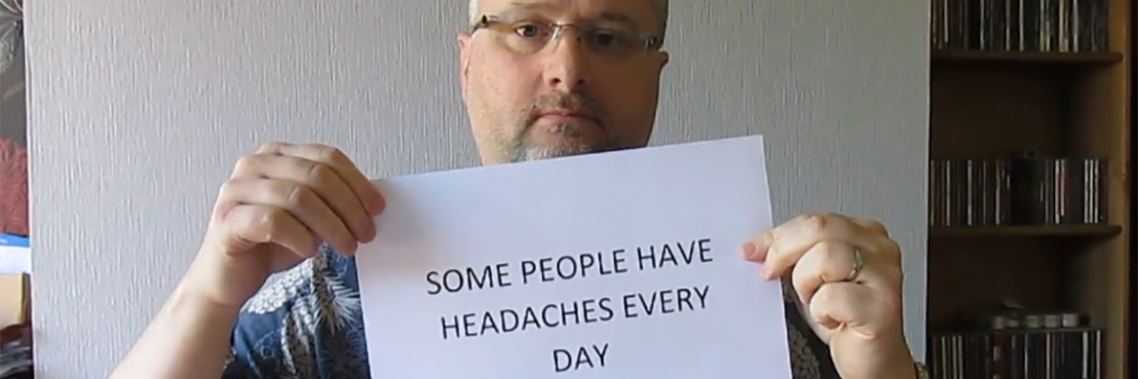 Living With Hidden Disability After a Brain Injury Andy holding a sign that says "Some people have headaches every day."