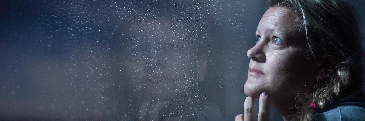 A Specialist's Tips for Managing Substance Use Urges During Pandemic A woman with braided blonde hair wearing a light blue sweatshirt looks pensively out the window