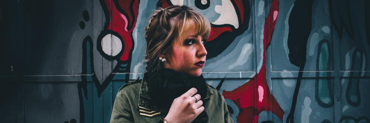 COVID-19 Limited My Coping Skills After My Psychiatric Hospital Stay A young white woman standing in front a mural outside bundled up looking away