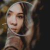 photo of woman looking into mirror reflection, focused on her reflection