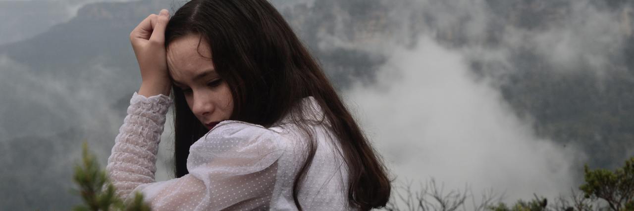 Decatastrophizing: How to Calm Down When the World Is Caving In photo of woman looking worried in front of misty mountains