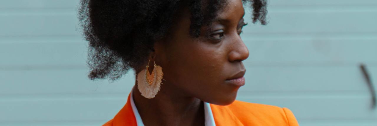 photo of a woman in an orange jacket in profile view against a light teal wall