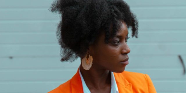How Systemic Racial Injustice and Trauma Leads to Bad Health Outcomes for Black People photo of a woman in an orange jacket in profile view against a light teal wall