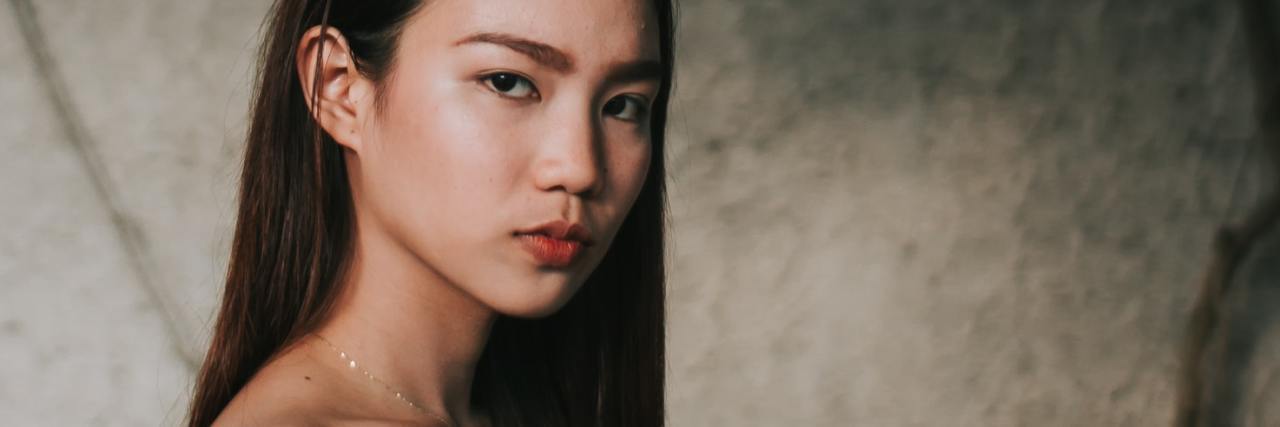 photo of young woman standing in front of concrete wall with ivy, looking into the camera with anger