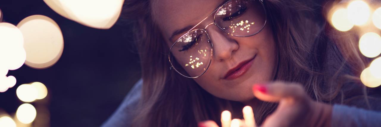 photo of woman with closed eyes, holding fairy lights in her hand and smiling