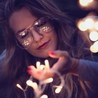 photo of woman with closed eyes, holding fairy lights in her hand and smiling