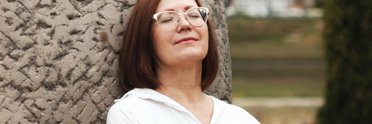 Bipolar Disorder and Trauma Triggers Don't Make Someone a 'Snowflake' photo of a woman with her eyes closed, arms folded, leaning her head back against a stone monument
