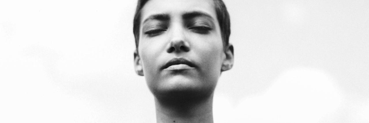 A black and white portrait of a woman with short hair closing her eyes, against a grey sky