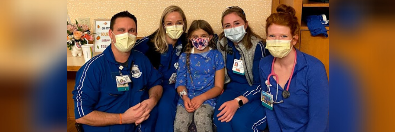 Photo of young girl surrounded by nurses, all wearing masks and smiling with their eyes