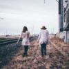 photo of two women walking along beside railroad track, close to each other