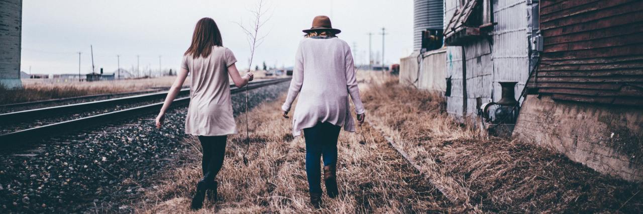 photo of two women walking along beside railroad track, close to each other
