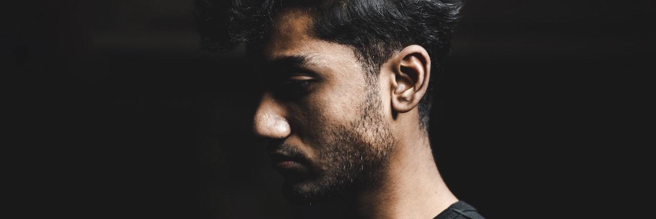 Does Mindfulness Meditation Work for Migraines? Profile of a man with dark hair wearing a black shirt who is hidden half in shadow