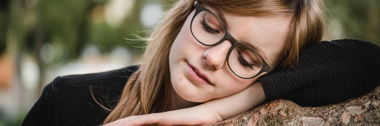 Why Giving Your Anxiety a Name Can Help You Cope photo of woman lying her arm and head on a branch with her eyes closed