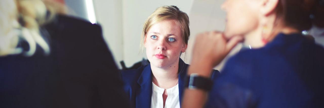 Real Negative Workplace Mental Health Experiences photo of three businesswomen in a meeting, two closer and out of focus, the third facing them like an interview