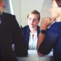 photo of three businesswomen in a meeting, two closer and out of focus, the third facing them like an interview