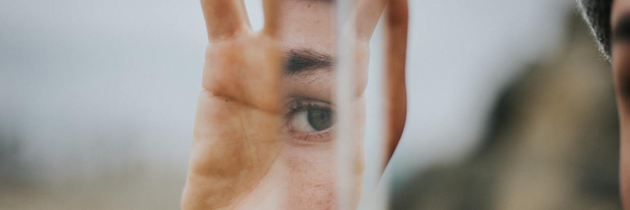 What to Know If You Think You Might Have Trauma a white hand holding a mirror with a girl's eye in the reflection