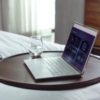 Open laptop alongside a glass of water on a wooden bed table