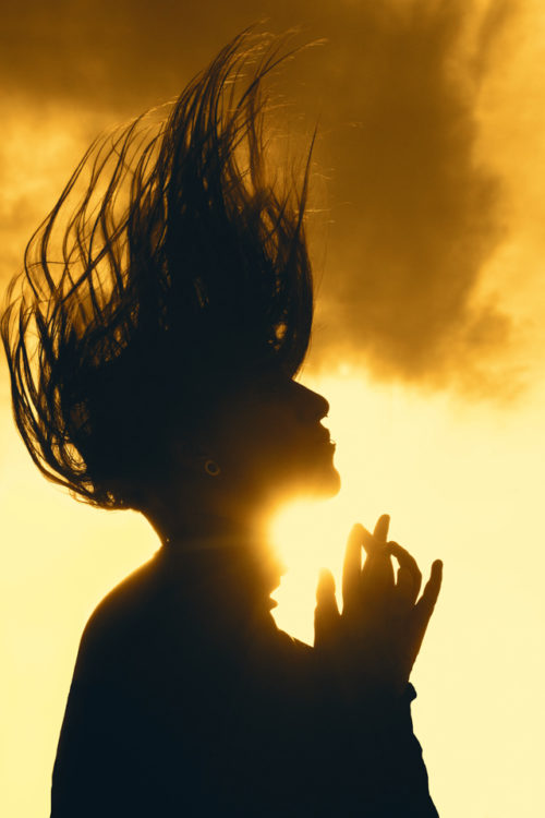 photo of author; young white woman with hair flying above her head as the sun shines on her face