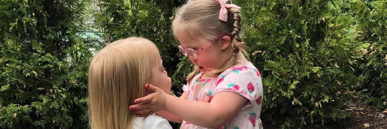 The Joy in the Journey of Raising a Child With Down Syndrome Toddler sisters embracing.