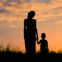 Mother and child silhouette walking in a field at sunset.