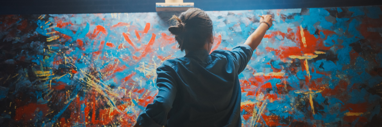 Using Art Therapy to Help Work Through Mental Illness Back of a young, white female artist painting abstractly on a large canvas