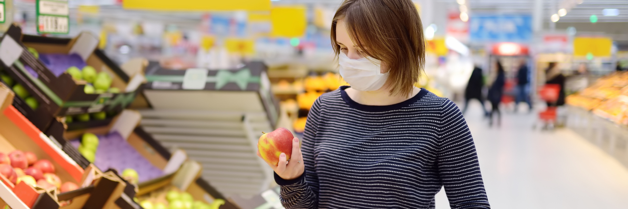 Grocery Shopping With Anxiety During COVID-19 a young woman with a face mask at a grocery store looking at fruit