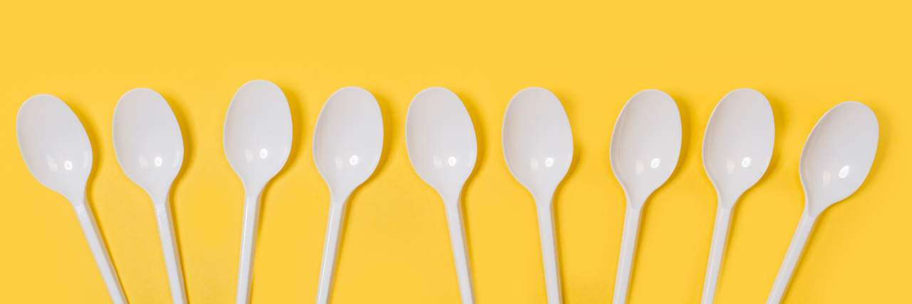 Disposable white plastic spoons on a yellow background.