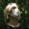 A woman facing the sun in a dark forest wearing a coronavirus mask during global pandemic.