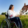 Woman sitting in her wheelchair, petting a horse.