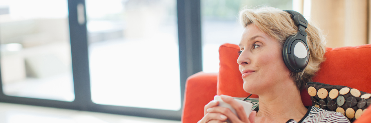 Songs That Help Me Cope With Chronic Illness Woman drinking coffee and listening to headphones.