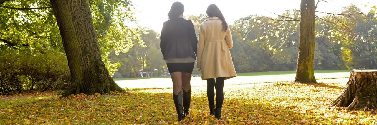 2 young women walking side-by-side through a field in the fall