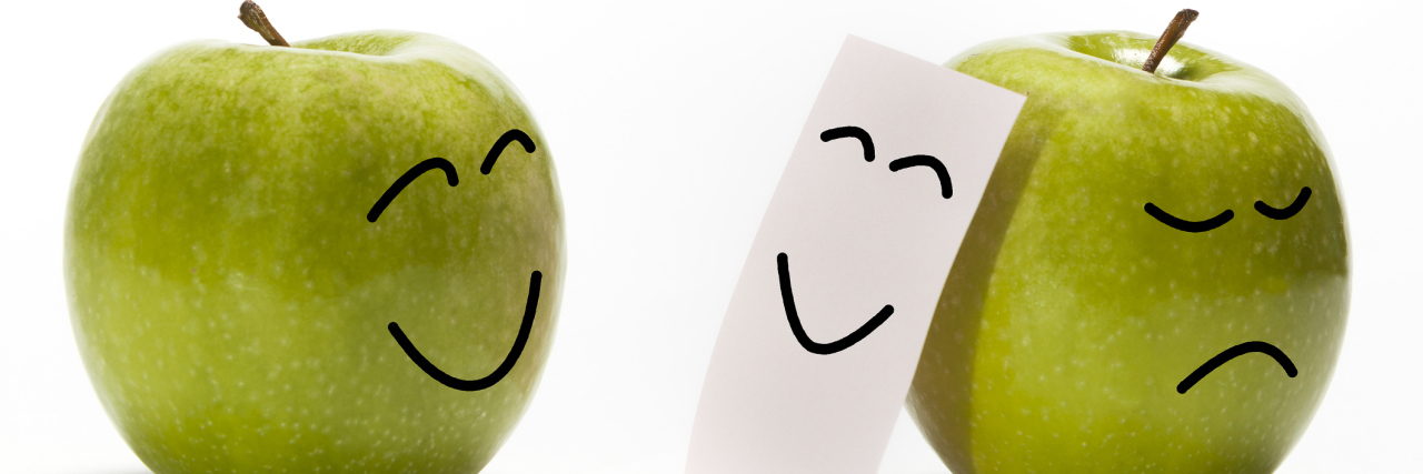 A green apple smiling at another green apple that is hiding its sad face with a smily mask