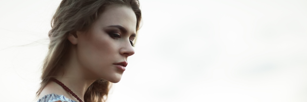 How to Speak Kindly to Yourself If You Struggle With Self-Criticism A young white woman with long blonde hair standing outside looking away