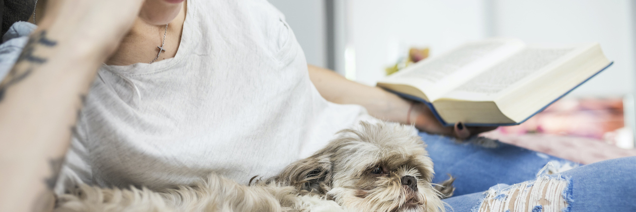 Life With My Dogs Has Helped Change My Perspective on Fibromyalgia Woman reading at home with her dog