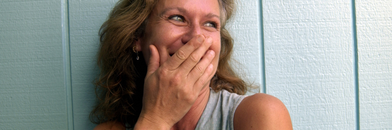 When Laughter Shows an End to Bipolar Depression May Be Coming photo of a woman laughing set against pastel blue green wooden background